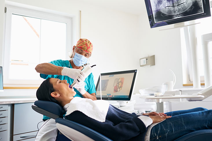 Zahnarzt Dr. Stephan Lindner scannt mit dem Intraoralscanner die Zähne einer Patientin.